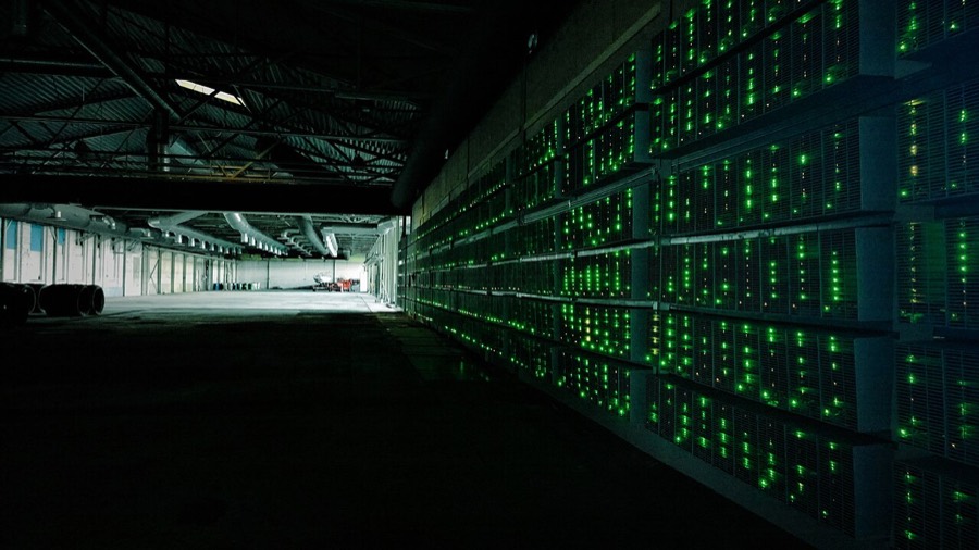 Rows of bitcoin mining machines with green lights inside a warehouse